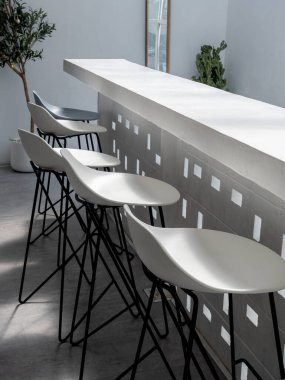 Boş beyaz bar sandalyeleri. Minimum beyaz restorandaki beyaz bar tezgahında modern koltuklar dikey olarak saksıya yakın..