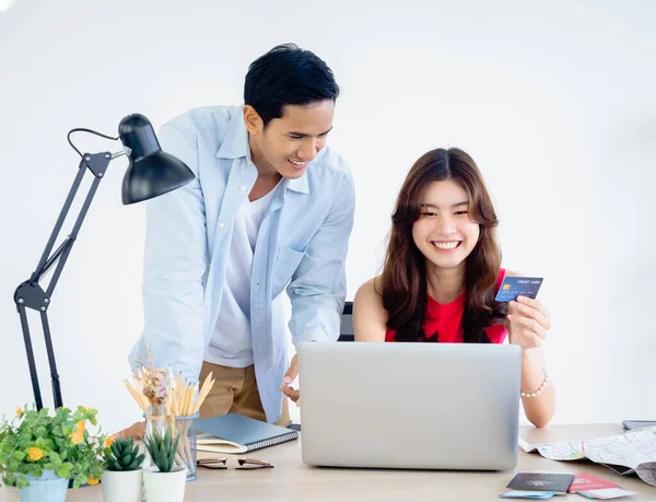 Young Asian couple, woman holding credit card and man happy after using laptop computer together for flight and hotel booking with success feeling for summer trip, ready to travel vacation concept.