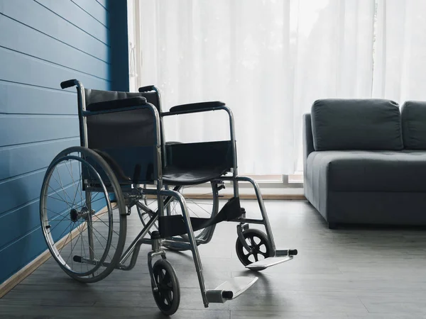 Empty Black Wheelchair Blue Wall Grey Sofa Seat White Curtain — Zdjęcie stockowe