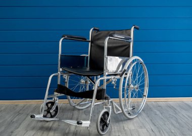 Siyah deri koltuklu, boş çelik tekerlekli sandalye ve mavi ahşap duvarlı arka planda sırt desteği. Yürüyemeyen, hastalıklı, yaralı bir kişinin taşımacılığı için tekerlekleri olan bir sandalye..