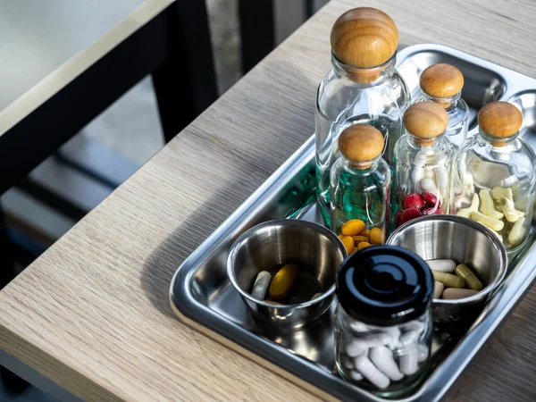 Close up set of vitamins and supplements in the small clear glass bottles in the steel medical tray on wooden table. Green, yellow, red, white vitamins group. Healthcare, and medical concepts.