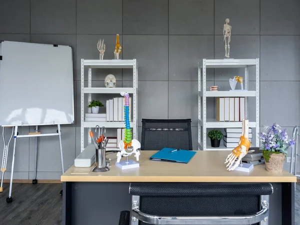 Orthopedic doctor office background decorated with chairs, table with tools and medical equipment, skeleton, bone model on shelf and white board. Interior of modern doctor\'s office in clinic.