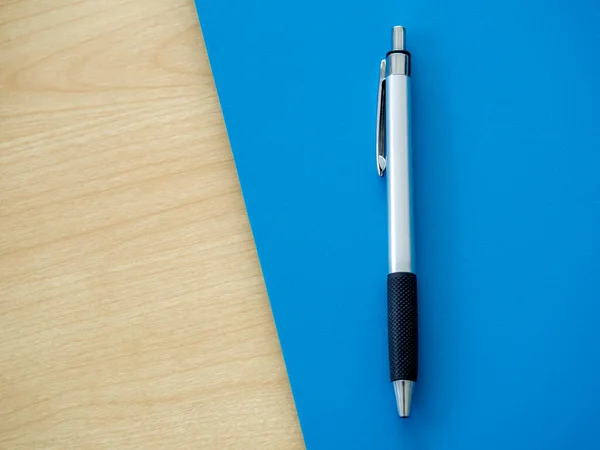 Silver ballpoint pen on blue and wooden background with copy space, top view. Flat lay of a metallic, steel, metal pen.