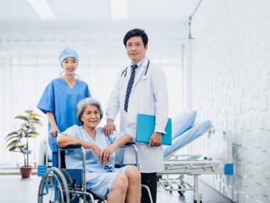 Male surgeon doctors and professional female nursing assistants take care senior woman patients in wheelchair near the bed in white clean recovering room in hospital. Health care and medical concept.