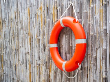 An orange lifebuoy, safety ring hanging on bamboo fence wall background with copy space. Rescue equipment. Lifesaver, Safety concepts.