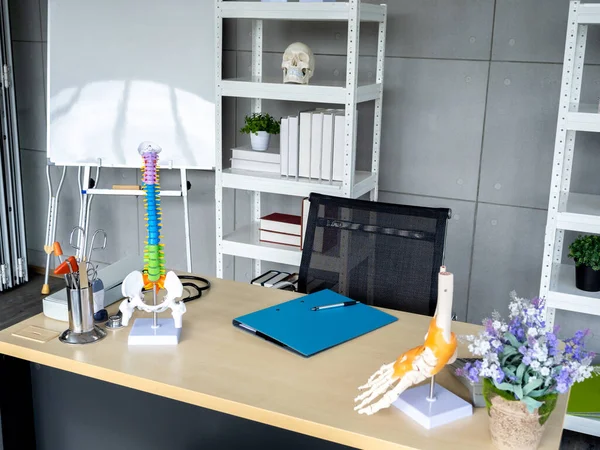 Orthopedic doctor office background decorated with folder file document, tools and medical equipment on table, skeleton model on shelf and white board. Interior of modern doctor's office in clinic.