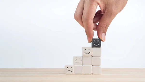 Feedback, client survey, customer experience satisfaction rating scale with emoticon face. Hand put the happy smile face on black cube on the top of white cube blocks on the growth chart steps.