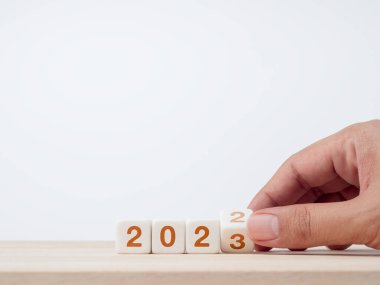 Close up hand flipping the 2022 to 2023 year numbers calendar on white cube blocks for preparation the new year change, begin and start new business target strategy and happy new year 2023 concept.