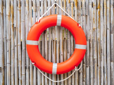 An orange lifebuoy, safety ring hanging on bamboo fence wall background, center view. Rescue equipment. Lifesaver, Safety concepts.