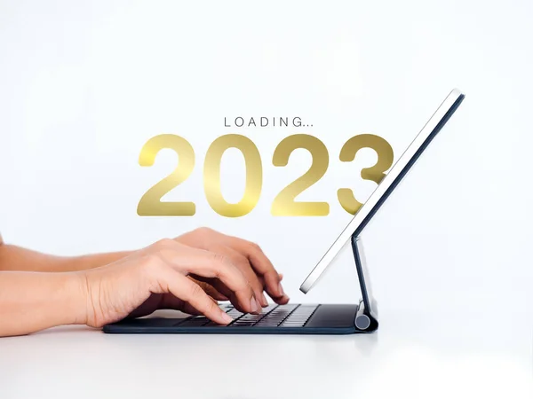 Loading to 2023 happy new year. 2023 year numbers calendar appear on digital tablet computer with hands typing it on white background to prepare for new year change and start new business technology.