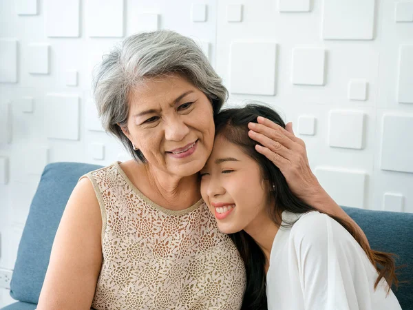 Portrait of happy Asian senior, mother white hair embracing her beautiful daughter with closing eyes with love, care, comfort and smile while sit on sofa on white background in living room at home.