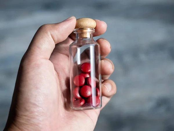 Close up red vitamins or supplements in the small clear glass bottle vials in person\'s hand. Hand holding vials with drug pills capsules. Healthcare, and medical concepts.