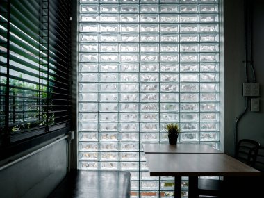 Glass brick wall background. Modern glass block wall with the light through decorated in the cafe with empty table and long bench seat, dim light room. Interior decor space wall in loft style concept.
