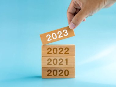 2023 Happy New year background. 2023 calendar numbers on wooden cube blocks stacked, building by hand isolated on blue background. Business planning, trends, goal, success, and vision concepts.