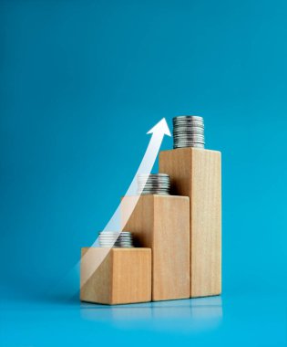 Shining rise up arrow on wooden cube blocks with coin stacked, bar graph chart steps on blue background, investment, profit, benefit, income, banking, business growth, economic improvement concepts.