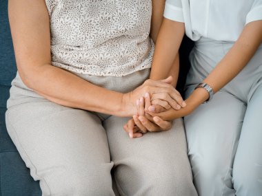 Close up of old mother, grandmother, elder or senior woman's hands hold her daughter or grandchild's hands for support with care and comfort. Giving love and encouragement concept.