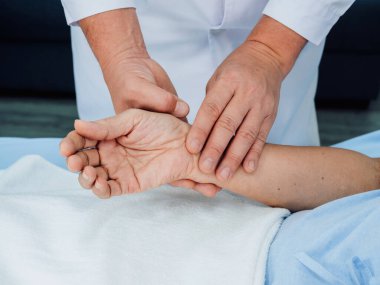 Hastanedeki iyileşme odasında kalp atışlarını kontrol etmek için yatakta yatan yaşlı bir hastanın elini tutan beyaz laboratuvar önlüğüyle doktorun elini kapat. Tıbbi kontrol kavramı.