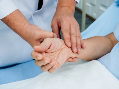 Hastanedeki iyileşme odasında kalp atışlarını kontrol etmek için yatakta yatan yaşlı bir hastanın elini tutan beyaz laboratuvar önlüğüyle doktorun elini kapat. Tıbbi kontrol kavramı.