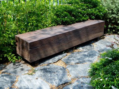 Boş koltuk, dikdörtgen şeklinde ahşap bir kütükten yapılmış. Güneşli bir günde ağaç gölgesi olan yeşil bahçedeki taş zemine yerleştirilmiş..