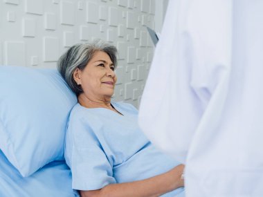 Sırıtkan Asyalı son sınıf öğrencisi gri saçlı hasta, genç bayan doktorlar geldiğinde iyileşiyor, hastane odasındaki semptomları, muayene notlarını ve tıbbi sağlık raporlarını açıklıyor.. 