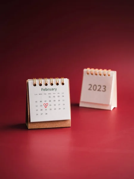 Happy Valentine's day, February 2023 calendar desk on red background, vertical style. Red heart draws hand mark on day 14 on white table calendar with the February month with the 2023 year numbers.