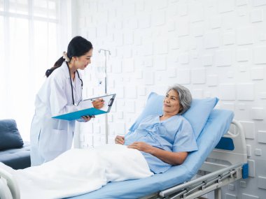 Sırıtkan Asyalı son sınıf öğrencisi gri saçlı hasta, genç bayan doktorlar geldiğinde iyileşiyor, hastane odasındaki semptomları, muayene notlarını ve tıbbi sağlık raporlarını açıklıyor.. 