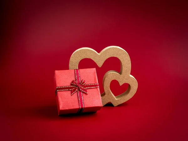 A small red present gift box with ribbon and wooden heart on red background. An essential gift with on special days with love, birthdays, New Years, Valentine's Day and anniversaries.