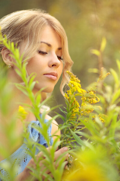 Beautiful caucasian girl in a blue dress smelling yellow wildflowers