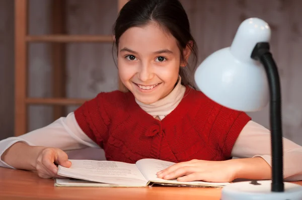 Mädchen am Schreibtisch liest ein Buch im Licht der Lampe — Stockfoto