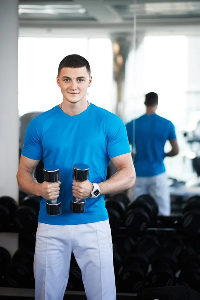 De jonge man in een sportschool met halters staat — Stockfoto