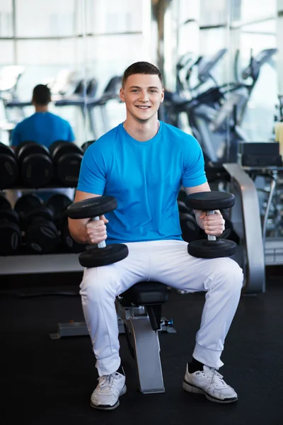 Young sports guy sitting on bench with a dumbbell — Stock fotografie