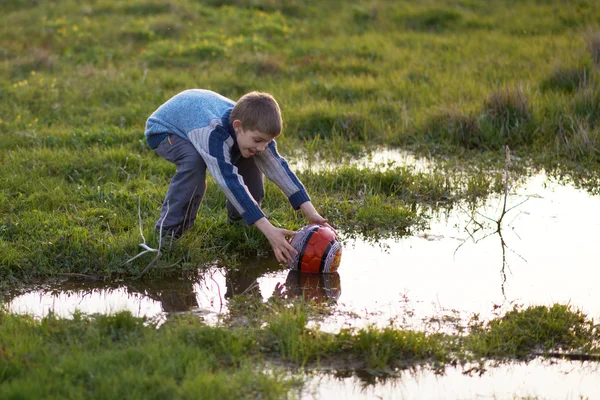 Chłopak dostaje piłkę z kałuże w trawie — Zdjęcie stockowe