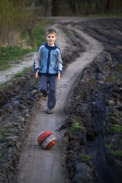 Chłopiec grający z piłką na drodze błoto — Zdjęcie stockowe