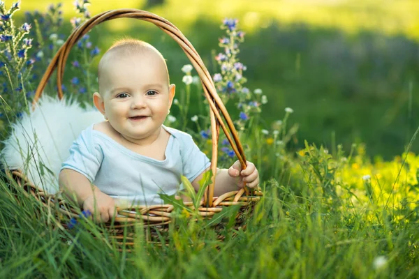 Маленький улыбающийся ребенок в ползунках, сидя в корзине — стоковое фото