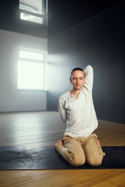 Bir adam eli arkada kilidin içinde oturur. Stüdyoda yoga çalışması..