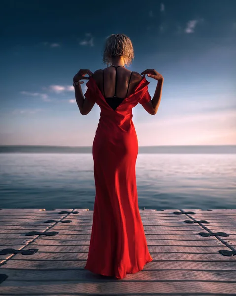 Atractiva joven con un vestido rojo desabotonado. Puesta de sol atmosférica en el muelle. —  Fotos de Stock