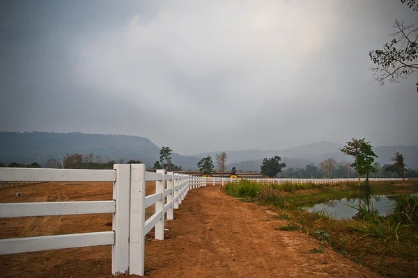 Cerca branca no campo de fazenda e céu nublado — Fotografia de Stock