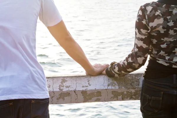 Pareja joven enamorada cogida de la mano mirando al atardecer — Foto de Stock