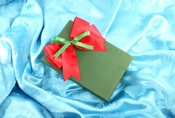 Green gift box with red ribbon on blue satin — Stock Photo, Image