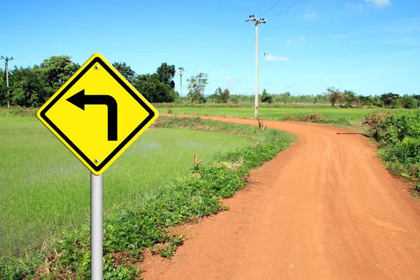 Turn left warning sign with soil road — Stok fotoğraf