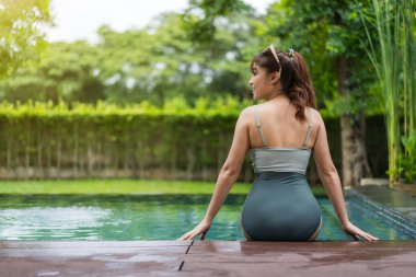 Yüzme havuzunun kenarında oturan genç bir kadın.