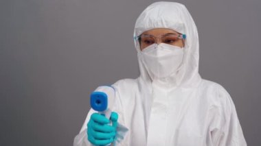 Koruyucu PPE giysili doktor kızılötesi termometreyle tarama yapıyor.