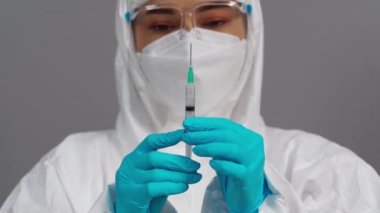 Korumalı PPE kıyafetli doktor Coronavirus (Covid-19) aşı enjeksiyon testi için şırınga tutuyor