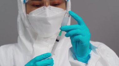 Koruyucu PPE kıyafetli doktor aşı şişesini şırınga ilacına çekiyor.
