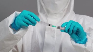Korumalı PPE kıyafetli doktor Coronavirus (Covid-19) aşı şişesini şırınga ilacına çiziyor