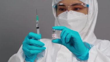 Coronavirus (Covid-19) aşı şişesi ve şırınga ilacı tutan koruyucu PPE kostümlü doktor