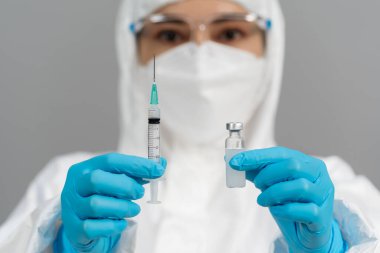Koruyucu PPE kıyafetli doktor elinde aşı şişesi ve şırınga ilacı tutuyor.