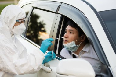 PPE giysi test koronavirüsü (covid-19) doktorundan, burun pamuğuyla arabada adama, hızlı test sürüşü yapın