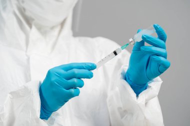 Koruyucu PPE kıyafetli doktor aşı şişesini şırınga ilacına çekiyor.