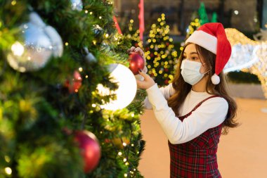 Tıbbi maskeli kadın ve Noel ağacı süsleme Noel Baba şapkası, koronavirüs (covid-19) ve X-mas kutlama konsepti